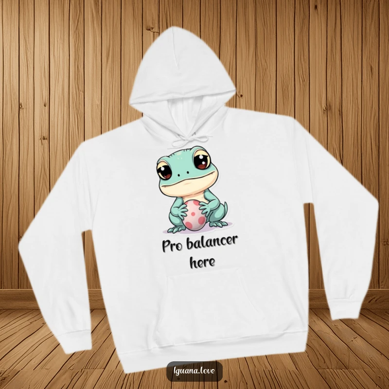 Funny hoodie featuring a kawaii iguana with wide eyes attempting to balance a tiny ball on its snout, radiating cuteness.